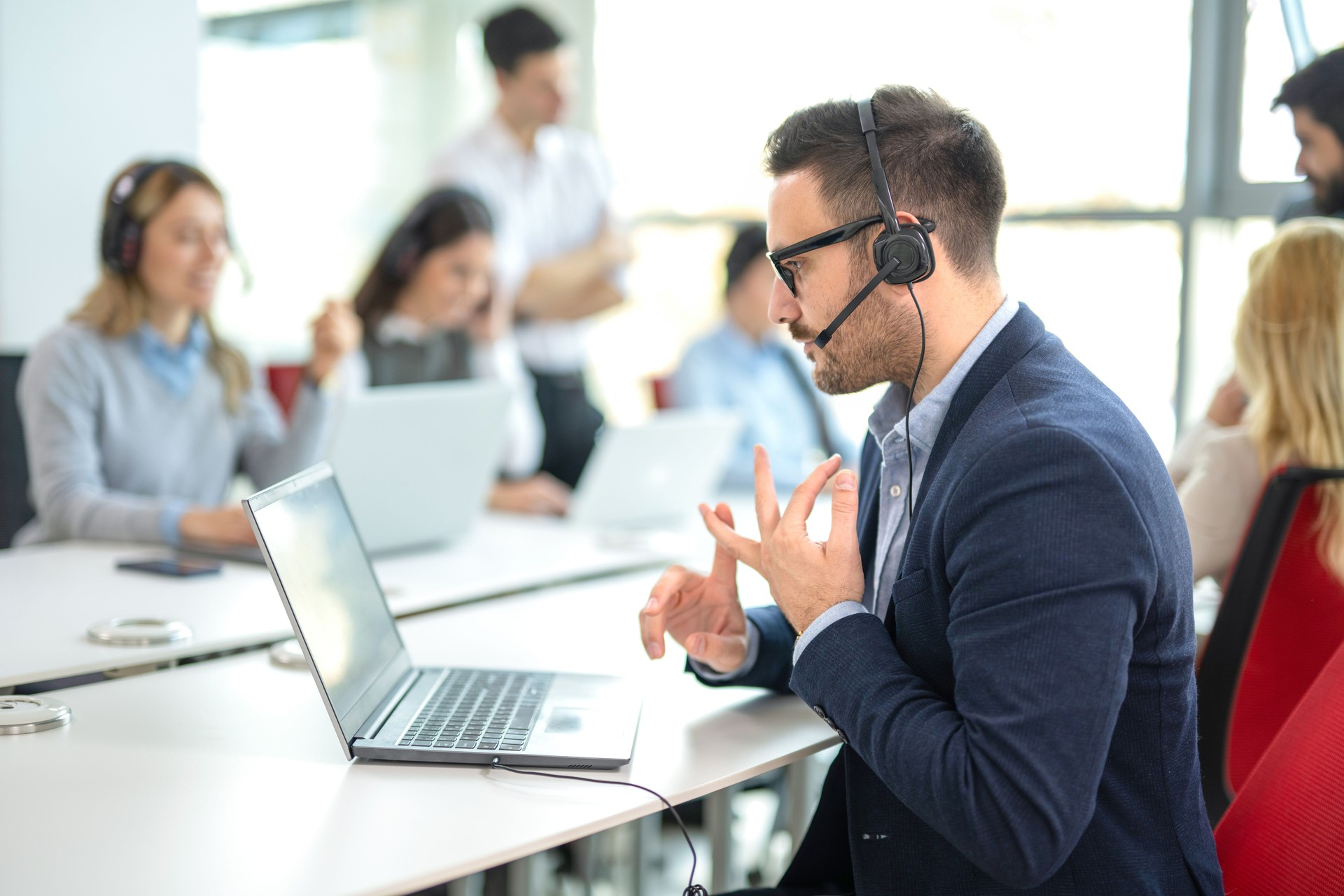 Professional customer support agent counting on his fingers while assisting customers at a call center office, with colleagues in the background.