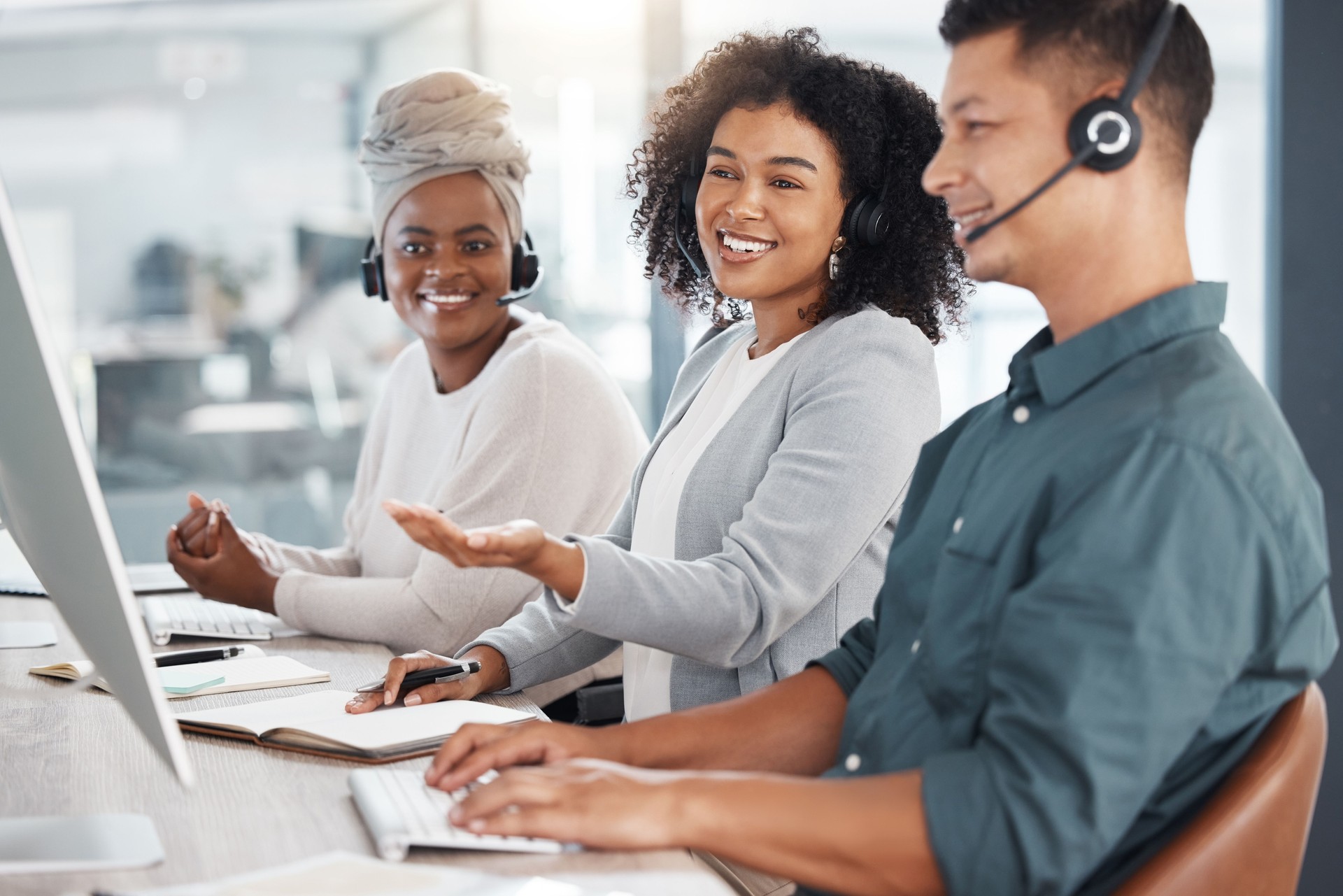 Young mixed race female call centre telemarketing agent discussing plans with colleagues while working together on a computer in an office. Consultants troubleshooting solution for customer service and sales support