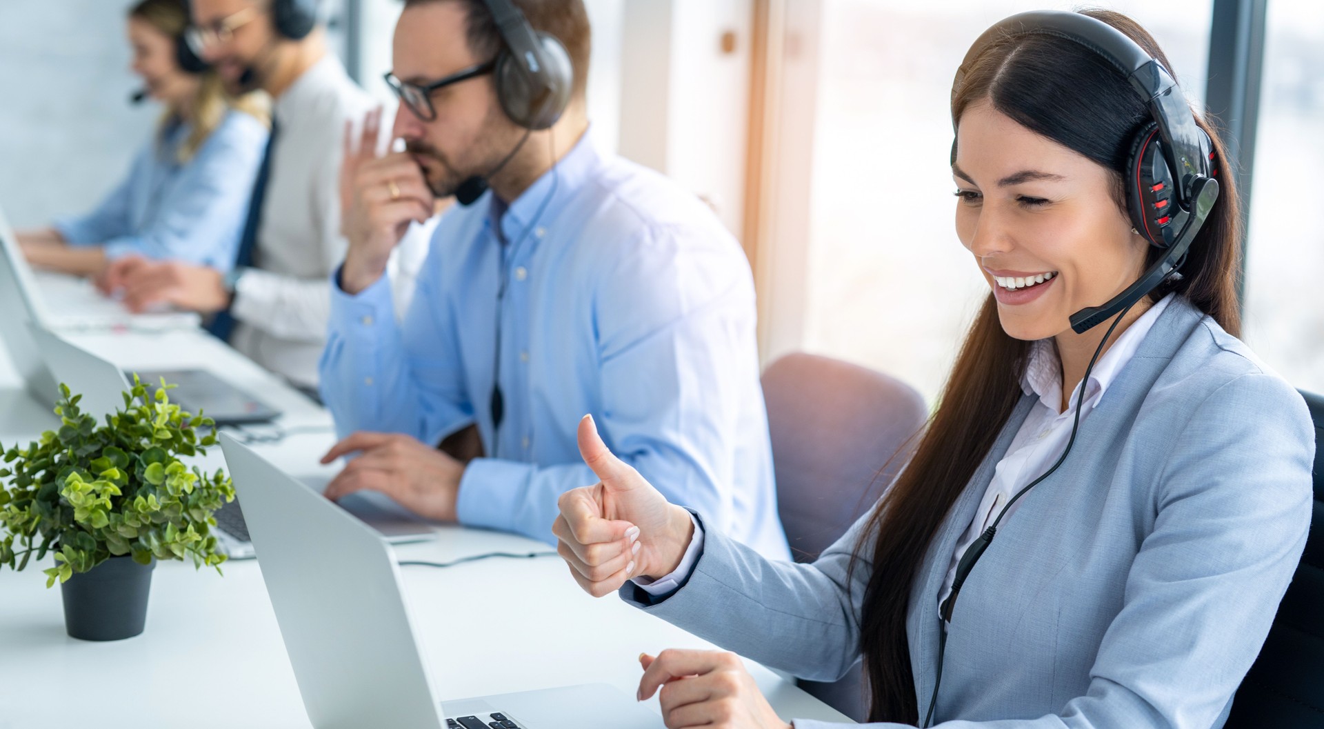 Woman operator showing thumbs up to computer screen while talking online on video call with customer at call center